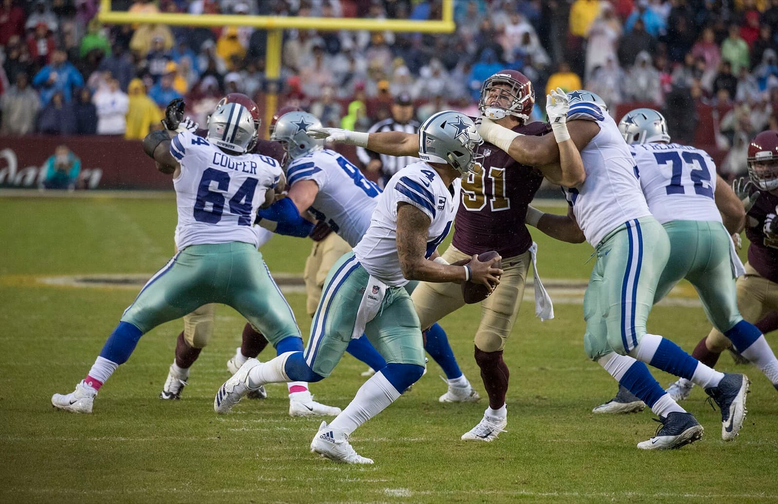 Dak Prescott, No. 4 in a white Cowboys uniform, throwing on the run as his linemen hold off a Washington pass rusher.